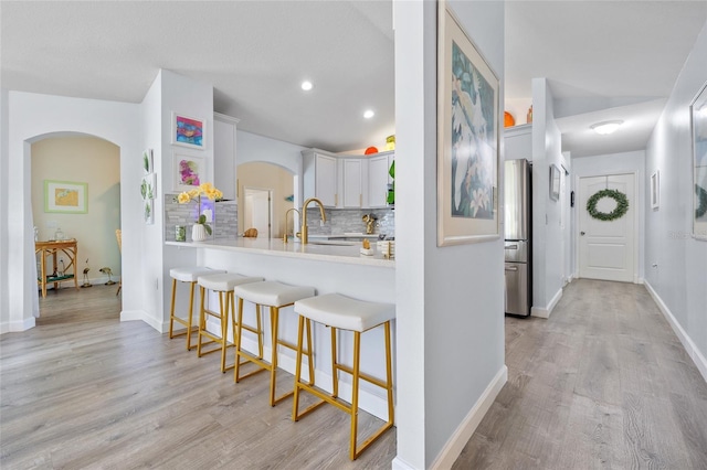 17396 Cox Ave, Port Charlotte, FL 33948 - kitchen with arched walkways, freestanding refrigerator, a kitchen bar, tasteful backsplash, and light wood-type flooring