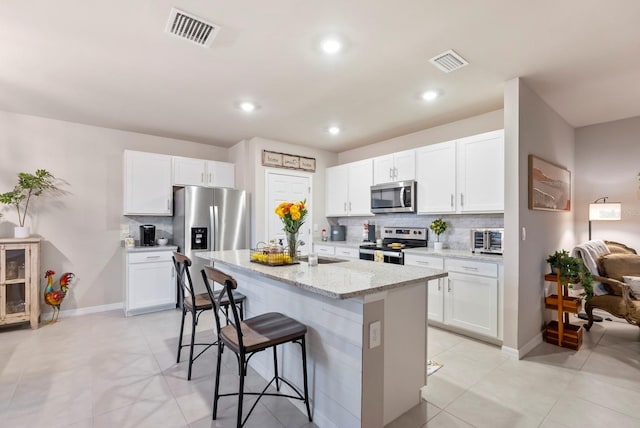 16032 Galiano Ct, Punta Gorda, FL 33955 - kitchen with appliances with stainless steel finishes, decorative backsplash, a breakfast bar area, light stone counters, and white cabinetry