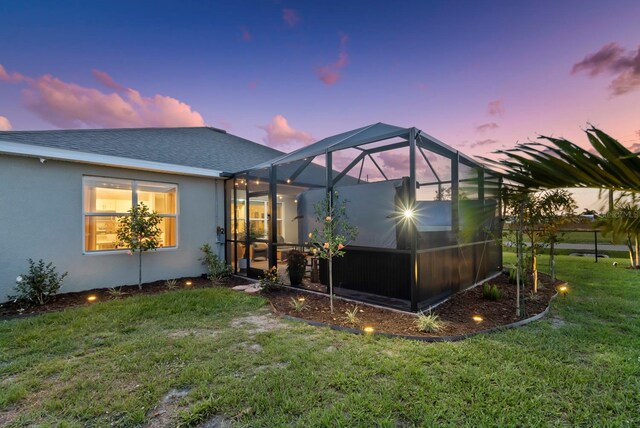 16032 Galiano Ct, Punta Gorda, FL 33955 - back of property at dusk featuring stucco siding, a lawn, glass enclosure, and roof with shingles