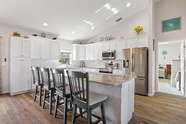 16094 Ortega Dr, Punta Gorda, FL 33955 - kitchen with appliances with stainless steel finishes, a breakfast bar, white cabinets, decorative backsplash, and light wood finished floors
