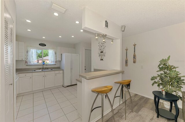 4044 S Salford Blvd, North Port, FL 34287 - kitchen featuring freestanding refrigerator, a sink, white cabinetry, a kitchen bar, and a peninsula