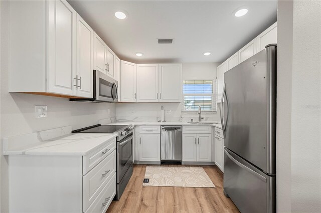 1080 Bal Harbor Blvd Unit 12C, Punta Gorda, FL 33950 - kitchen with stainless steel appliances, a sink, light wood finished floors, white cabinetry, and light stone countertops