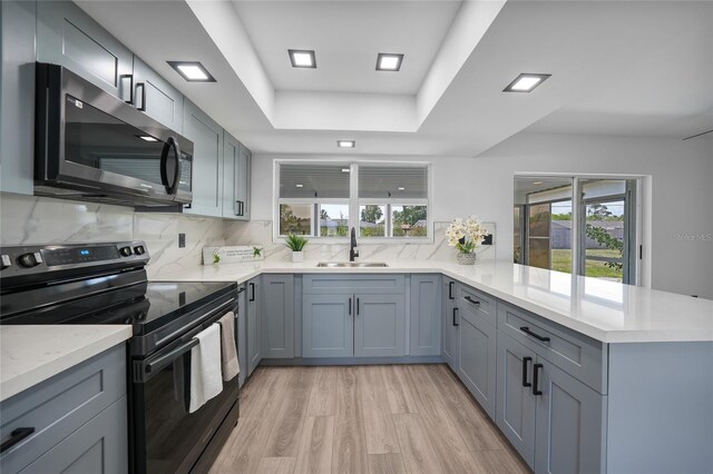 2166 Beacon Dr, Port Charlotte, FL 33952 - kitchen featuring black electric range oven, a sink, a peninsula, light wood finished floors, and decorative backsplash