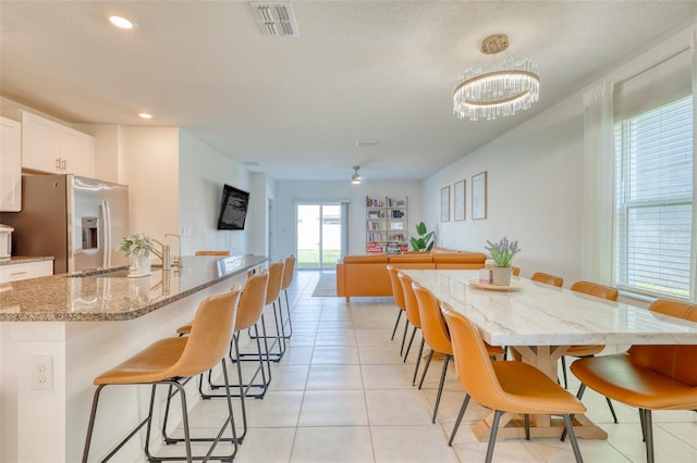 111 Rain Lily Ave, Spring Hill, FL 34609 - kitchen featuring stainless steel fridge with ice dispenser, a breakfast bar area, white cabinetry, an island with sink, and light stone counters