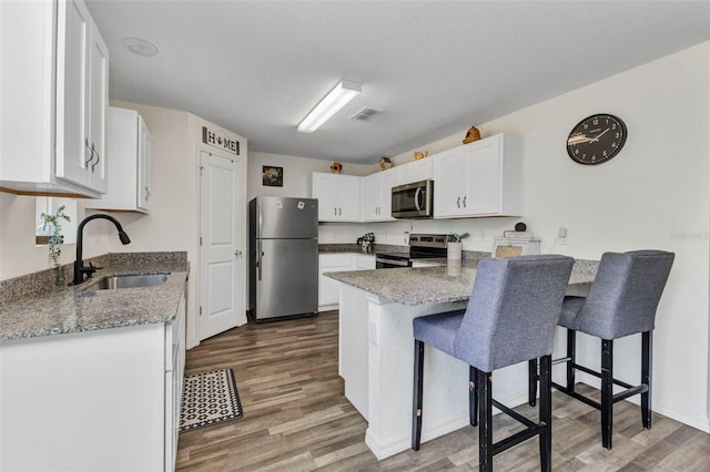 3799 Laredo Ave, North Port, FL 34288 - kitchen with stainless steel appliances, a sink, a peninsula, white cabinets, and wood finished floors