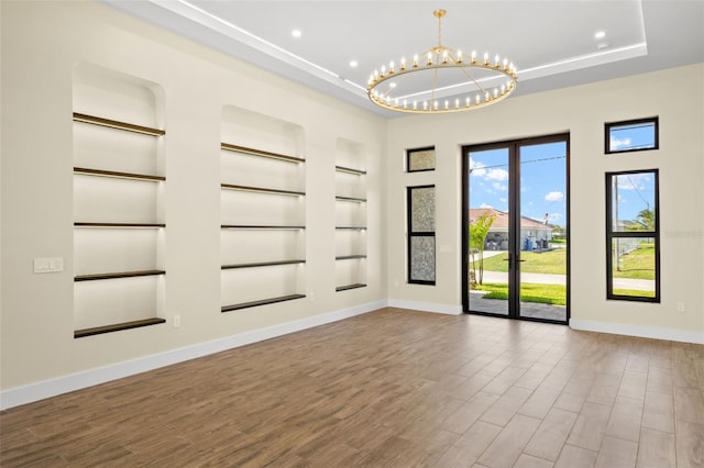 3413 NW 9th Ter, Cape Coral, FL 33904 - empty room featuring a tray ceiling, built in features, baseboards, a chandelier, and wood finished floors