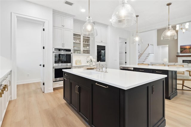 3632 Golden Gate Blvd W, Naples, FL 34102 - kitchen with a kitchen island, double oven, a sink, white cabinetry, and light wood-type flooring