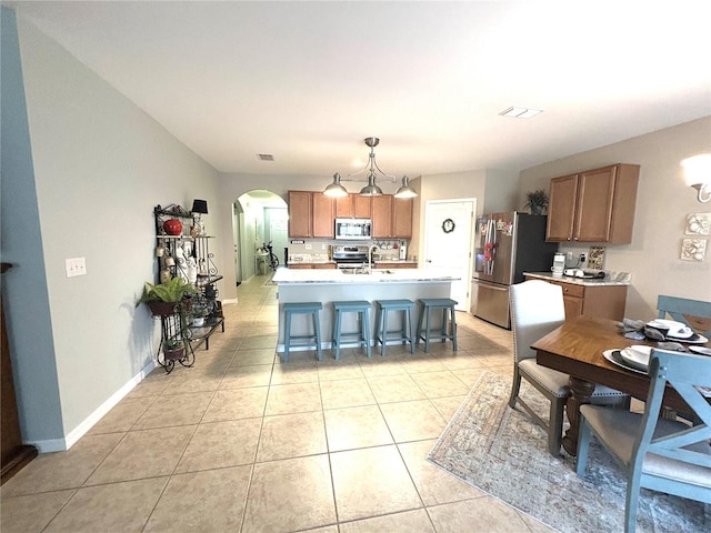 25008 Lalique Pl, Punta Gorda, FL 33950 - kitchen featuring stainless steel appliances, arched walkways, light countertops, light tile patterned floors, and a kitchen bar