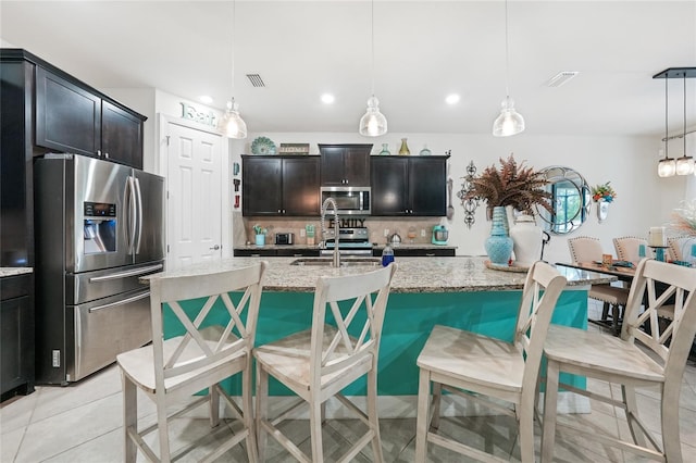 2515 Sherman Oak Dr, North Port, FL 34289 - kitchen with appliances with stainless steel finishes, decorative backsplash, light stone counters, a center island with sink, and a kitchen bar