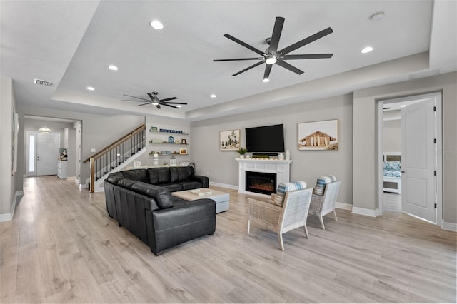 19821 Montenero Way, Venice, FL 34293 - living room featuring a raised ceiling, a ceiling fan, a warm lit fireplace, baseboards, and light wood-style flooring