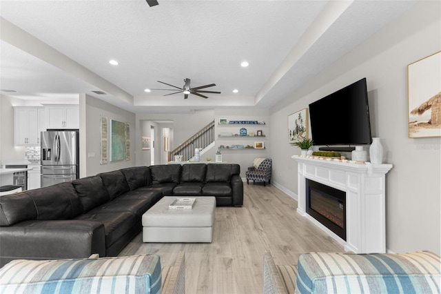 19821 Montenero Way, Venice, FL 34293 - living area with a ceiling fan, a raised ceiling, stairway, light wood-style flooring, and a glass covered fireplace