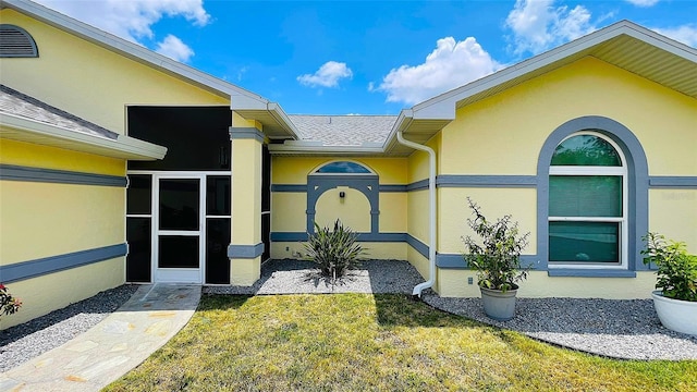 2399 Bendway Dr, Port Charlotte, FL 33948 - view of exterior entry featuring a yard, stucco siding, and roof with shingles