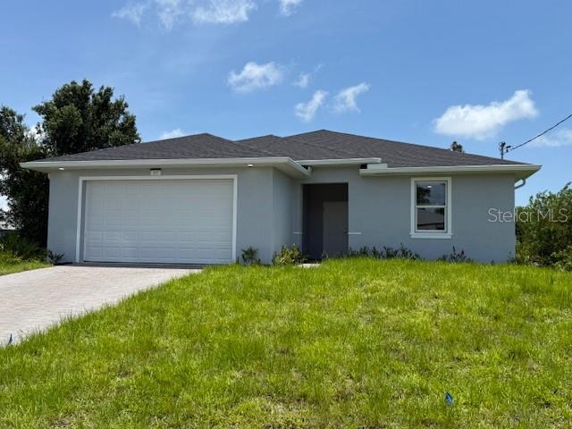 207 Baytree Dr, Rotonda West, FL 33947 - view of front of home featuring stucco siding, an attached garage, driveway, and a front lawn
