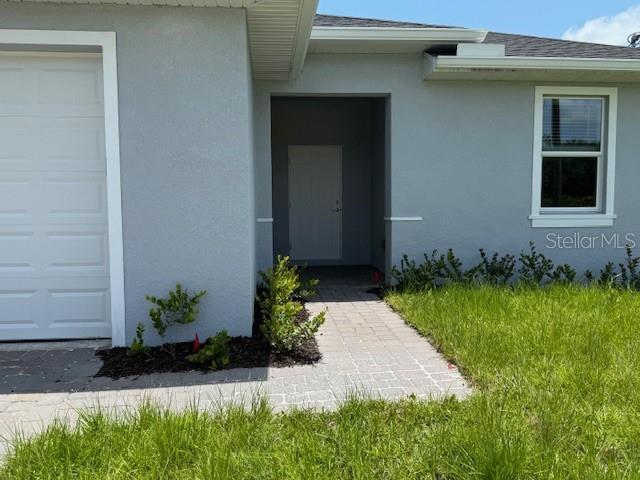207 Baytree Dr, Rotonda West, FL 33947 - doorway to property featuring a garage, stucco siding, and a shingled roof