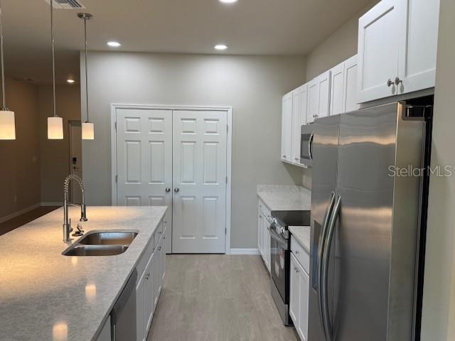 207 Baytree Dr, Rotonda West, FL 33947 - kitchen featuring stainless steel appliances, a sink, light stone countertops, white cabinets, and light wood-style floors