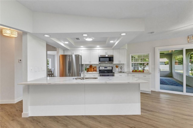 229 Waterside St, Port Charlotte, FL 33954 - kitchen featuring appliances with stainless steel finishes, a raised ceiling, white cabinets, light wood-style floors, and decorative backsplash