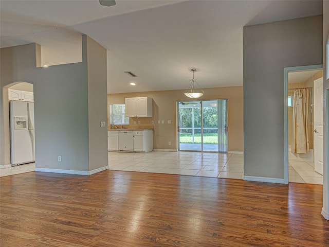 4609 Jaslo Ave, North Port, FL 34286 - unfurnished living room featuring arched walkways, vaulted ceiling, light wood finished floors, baseboards, and a sink