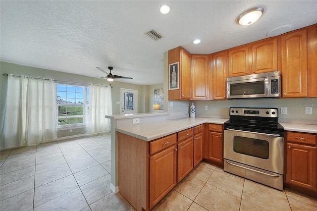 3171 Highlands Rd, Punta Gorda, FL 33983 - kitchen with appliances with stainless steel finishes, a peninsula, light countertops, brown cabinets, and light tile patterned flooring
