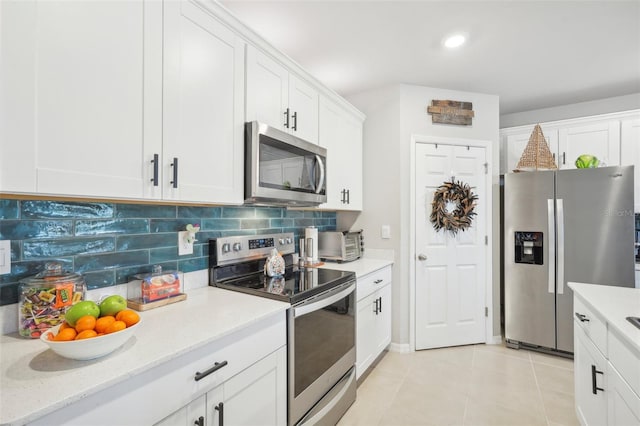 kitchen featuring stainless steel appliances, backsplash, white cabinetry, light tile patterned floors, and light stone countertops