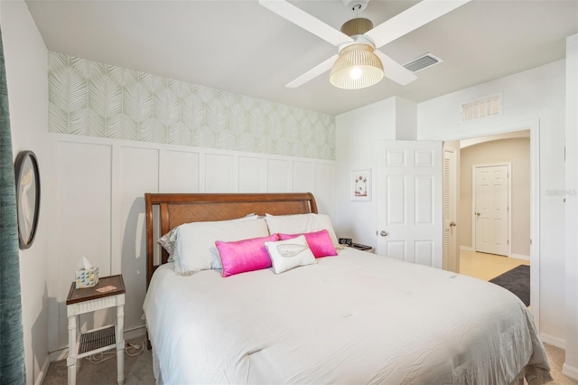 carpeted bedroom featuring a decorative wall, ceiling fan, baseboards, and a wainscoted wall