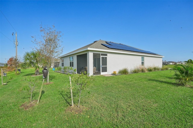 back of property featuring solar panels, a lawn, a sunroom, and stucco siding