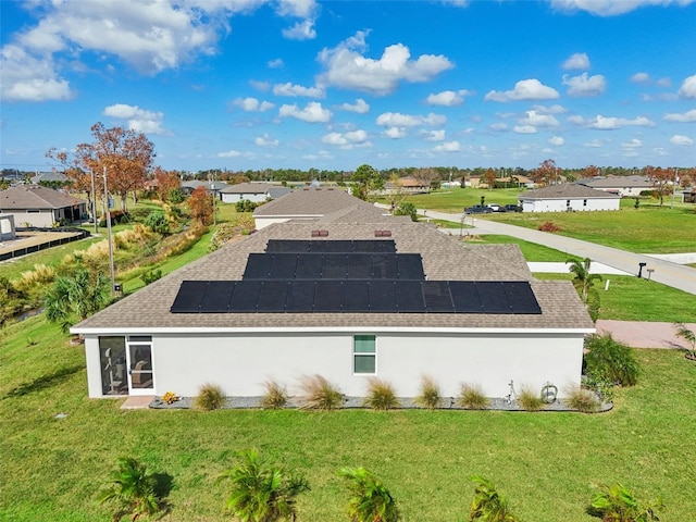 view of side of home featuring a residential view, a shingled roof, solar panels, and a yard