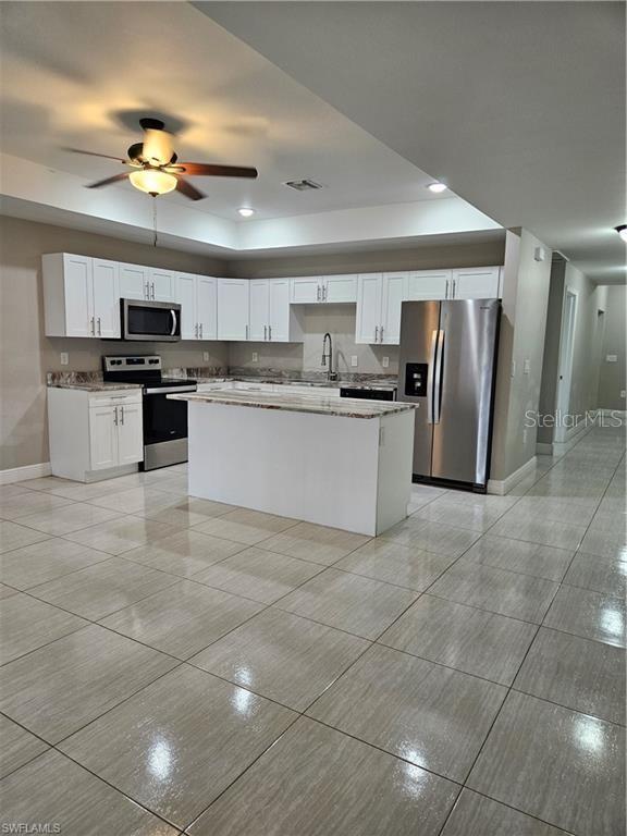 4916/4918 24th St SW, Lehigh Acres, FL 33973 - kitchen featuring stainless steel appliances, baseboards, light tile patterned flooring, a kitchen island, and white cabinetry