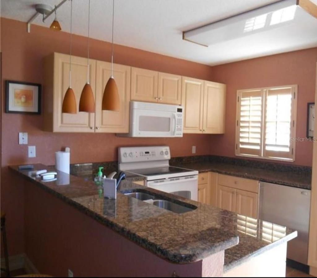 25050 Sandhill Blvd Unit A2, Punta Gorda, FL 33983 - kitchen with white appliances, a peninsula, dark stone counters, decorative light fixtures, and a sink