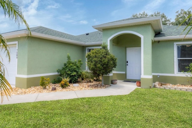 7280 Muncey Rd, North Port, FL 34291 - view of exterior entry with a shingled roof, a yard, stucco siding, and an attached garage