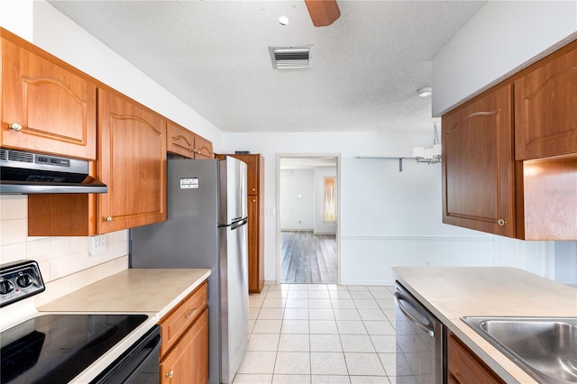 3242 Nocturne Rd, Venice, FL 34293 - kitchen featuring under cabinet range hood, stainless steel appliances, decorative backsplash, brown cabinetry, and a textured ceiling