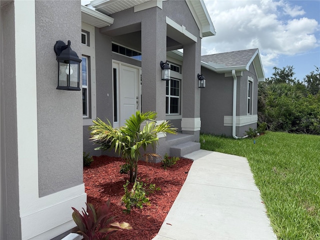 10023 Greetings St, Port Charlotte, FL 33981 - doorway to property featuring stucco siding, a yard, and a shingled roof