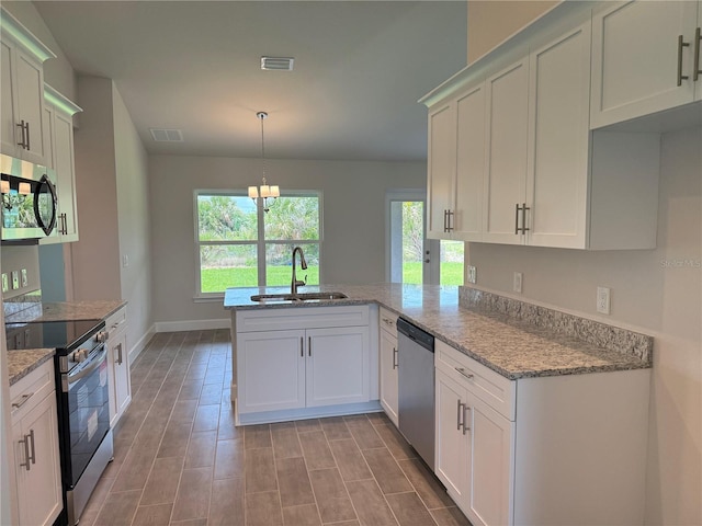 10023 Greetings St, Port Charlotte, FL 33981 - kitchen with stainless steel appliances, a peninsula, light stone counters, hanging light fixtures, and white cabinets