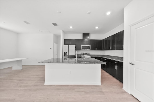 2138 Blaser St, Punta Gorda, FL 33980 - kitchen featuring appliances with stainless steel finishes, dark cabinets, a kitchen island with sink, stone countertops, and light wood finished floors