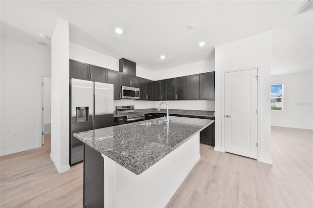 2138 Blaser St, Punta Gorda, FL 33980 - kitchen with stainless steel appliances, light wood finished floors, dark stone countertops, dark cabinets, and a kitchen island with sink