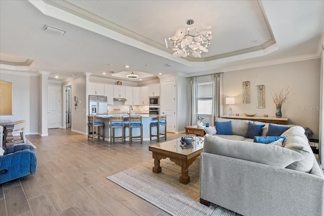 15039 Black Cherry Way, Punta Gorda, FL 33955 - living room featuring a tray ceiling, crown molding, light wood-style floors, a chandelier, and ornate columns