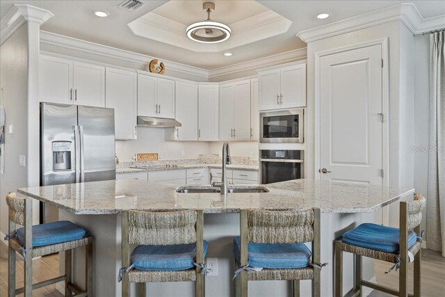 15039 Black Cherry Way, Punta Gorda, FL 33955 - kitchen with under cabinet range hood, stainless steel appliances, white cabinetry, crown molding, and a kitchen bar