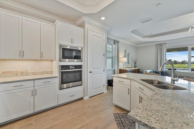15039 Black Cherry Way, Punta Gorda, FL 33955 - kitchen with appliances with stainless steel finishes, a tray ceiling, ornamental molding, light wood-style flooring, and white cabinetry