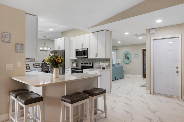 1141 Paraclete Rd, Punta Gorda, FL 33983 - kitchen with stainless steel appliances, a breakfast bar area, light marble finish floors, a peninsula, and white cabinets