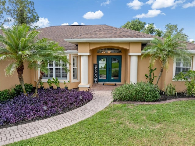 2373 Chartwell Ave, North Port, FL 34288 - view of exterior entry featuring french doors, stucco siding, a yard, and a shingled roof
