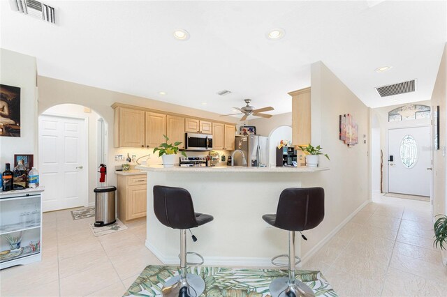 167 Marker Rd, Rotonda West, FL 33947 - kitchen with stainless steel appliances, light brown cabinetry, arched walkways, a kitchen bar, and light tile patterned floors