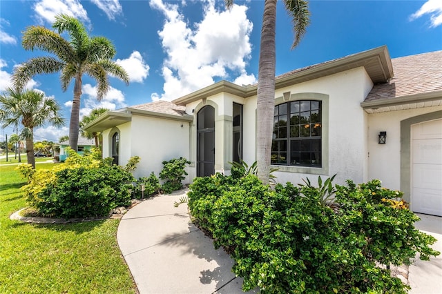 167 Marker Rd, Rotonda West, FL 33947 - property entrance featuring stucco siding, a garage, roof with shingles, and a lawn