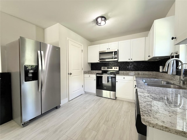 17344 York Ave, Port Charlotte, FL 33948 - kitchen featuring appliances with stainless steel finishes, light stone counters, light wood-type flooring, white cabinetry, and decorative backsplash
