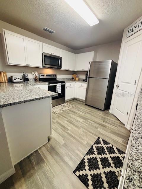 6766 N Pavilion Loop, Citrus Springs, FL 34433 - kitchen featuring stainless steel appliances, a textured ceiling, light wood-style flooring, a peninsula, and white cabinetry