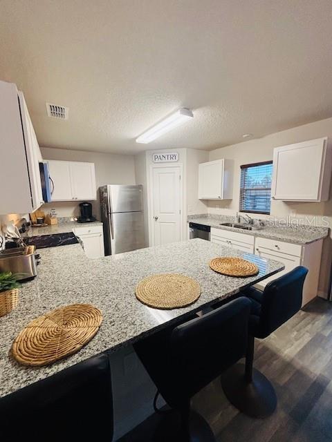 6766 N Pavilion Loop, Citrus Springs, FL 34433 - kitchen featuring stainless steel appliances, a peninsula, a breakfast bar area, dark wood finished floors, and white cabinets