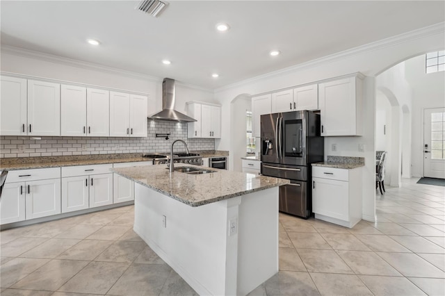11105 Balfour St E, Venice, FL 34293 - kitchen featuring stainless steel fridge with ice dispenser, wall chimney range hood, arched walkways, light tile patterned floors, and crown molding