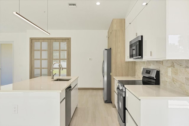 4530 Boston Ter, North Port, FL 34288 - kitchen featuring appliances with stainless steel finishes, a kitchen island with sink, decorative backsplash, light countertops, and white cabinetry