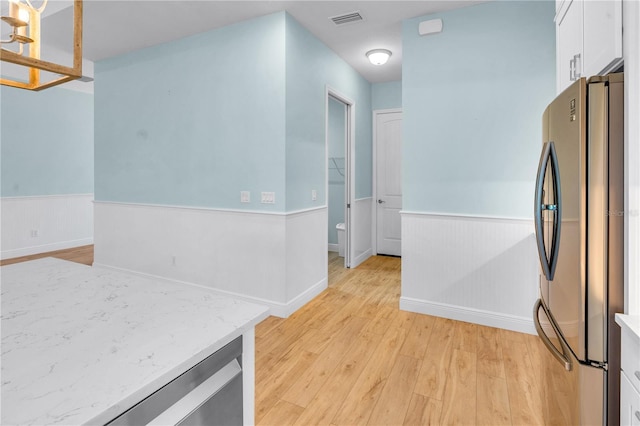10478 Coquina Ct, Placida, FL 33946 - kitchen featuring freestanding refrigerator, white cabinets, a wainscoted wall, light wood-style floors, and light stone counters