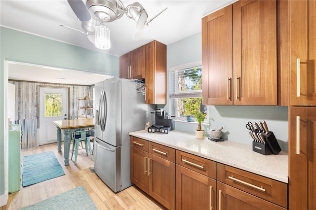 1027 Coral Ridge Dr, Punta Gorda, FL 33950 - kitchen featuring stainless steel fridge with ice dispenser, brown cabinetry, light wood finished floors, light stone countertops, and ceiling fan