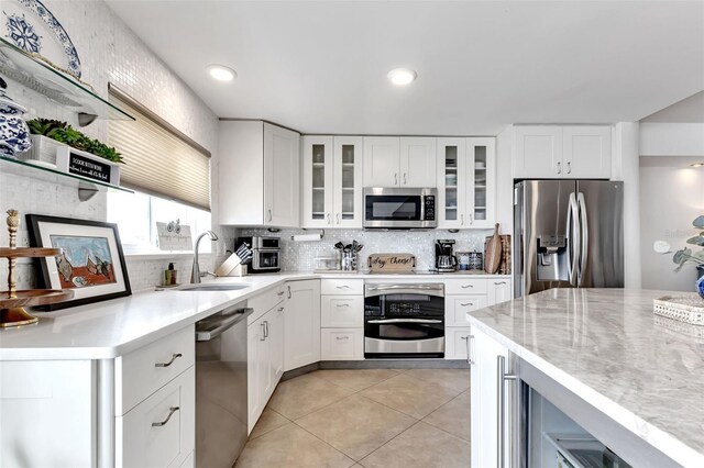 1250 W Marion Ave Unit 333, Punta Gorda, FL 33950 - kitchen with appliances with stainless steel finishes, decorative backsplash, light tile patterned flooring, glass insert cabinets, and white cabinetry