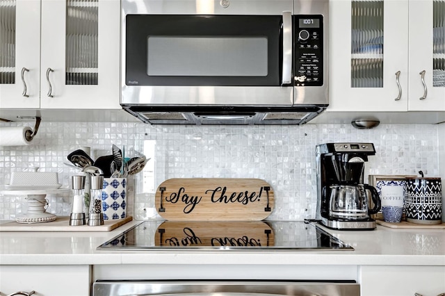 1250 W Marion Ave Unit 333, Punta Gorda, FL 33950 - kitchen view of stainless steel microwave, tasteful backsplash, white cabinetry, black electric cooktop, and light countertops